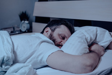 A lonely bearded dark-haired man sleeps soundly on his stomach at night on the bed. Close-up, pillow, bedroom, self-isolation.