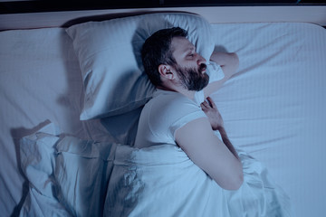 A lonely bearded dark-haired man sleeps soundly on his left side at night in bed. Close-up from...