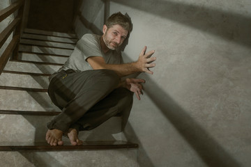 horror movie style portrait of sad and desperate man suffering depression problem or mental disorder sitting on staircase at home hopeless crying overwhelmed