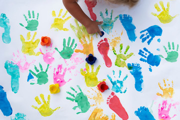Sensory play of children. Little child imprint colorful palm and foot on white background. Hand of girl paints artictic artwork. Childhood and colors of fun.