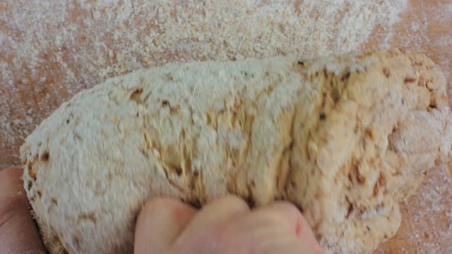 A 4K close up shot of a woman kneading some dough and making some bread. Using hands to make a loaf of bread on a wooden board with flour surrounding it.