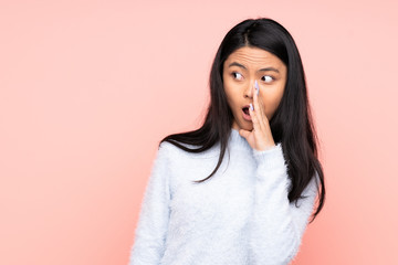 Teenager Chinese woman isolated on pink background whispering something with surprise gesture while looking to the side