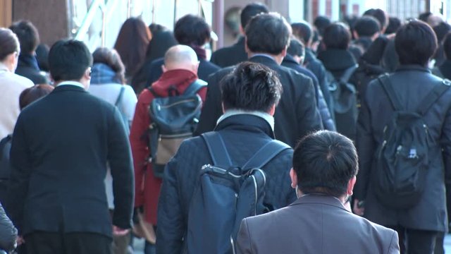 TOKYO, JAPAN - MARCH 2020 : View of crowd of people walking down the street in busy morning rush hour. Many commuters going to work. Japanese business, job and lifestyle concept. Slow motion shot.
