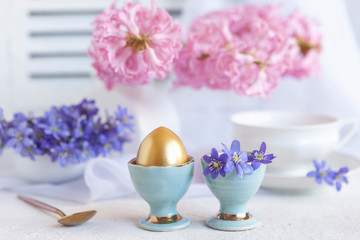 Fresh bouquet of delicate spring flowers liverwort Hepatica Nobilis and a golden egg in an egg stand - breakfast for Easter morning
