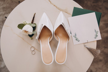 white designer women's shoes stand next to invitation cards and wedding rings, wedding details of the bride