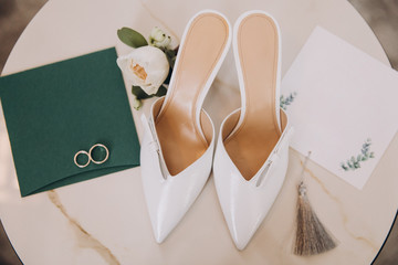 white designer women's shoes stand next to invitation cards and wedding rings, wedding details of the bride