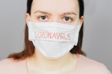 Young girl in medical mask with the text Coronavirus on a gray background. Pandemic, an epidemic in the world. Emotions