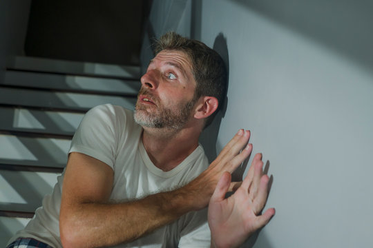 horror movie style portrait of sad and desperate man suffering depression problem or mental disorder sitting on staircase at home hopeless crying overwhelmed