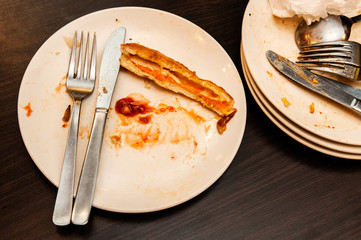 Leftover food in white plate with cutlery on wooden table