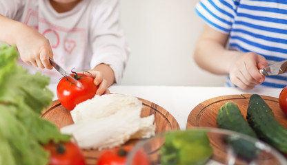 Happy children prepares vegetables for salad in home kitchen. Healthy eating.