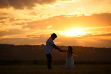 Fototapeta na wymiar silhouette of dad and daughter in field at sunset.