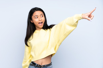 Teenager Chinese woman isolated on blue background pointing away