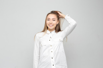 Obraz premium Beautiful young woman portrait. Portrait of a beautiful smiling blonde in white shirt on a white-gray. woman straightens her hair or holds her head