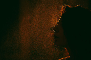 dark female head silhouette with wet hair against a background of orange light with splashes of...
