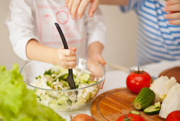 Happy children prepares vegetables for salad in home kitchen. Healthy eating.
