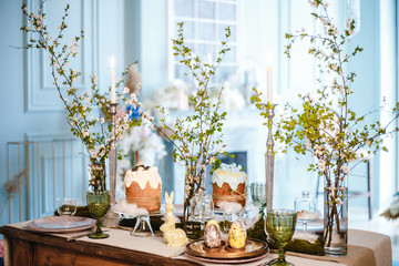 table decorated for Easter: Easter cakes, Easter eggs, Easter bunnies, flowering cherry branches in glass cups, plates and glasses
