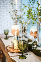 table decorated for Easter: Easter cakes, Easter eggs, Easter bunnies, flowering cherry branches in glass cups, plates and glasses