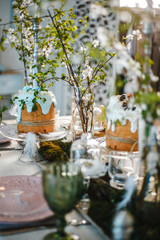 table decorated for Easter: Easter cakes, Easter eggs, Easter bunnies, flowering cherry branches in glass cups, plates and glasses