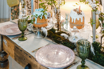 table decorated for Easter: Easter cakes, Easter eggs, Easter bunnies, flowering cherry branches in glass cups, plates and glasses