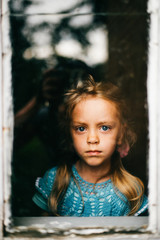 Lonely abandoned unhappy little girl looking through window with abstract reflections. Kid...