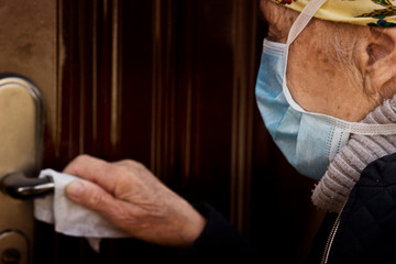 An old grandmother touches a door handle with an antiseptic wipe to prevent infection with a coronavirus infection. Quarantine safety measures for an outbreak of coronavirus.