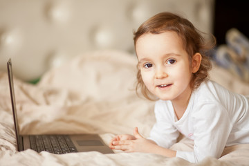 Little cute girl lying on the bed and using a digital tablet laptop notebook.