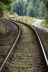 Railway curve and asphalt winding road in a forest. Two communication and transport routes lying next to each other