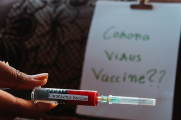 Hand holding an injection containing the Corona Virus vaccine in front of research paper