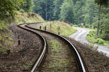 Railway curve and asphalt winding road in a green forest. Two communication and transport routes lying next to each other