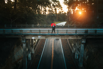 Person alone on bridge that is deserted over a deserted road with a red umbrella