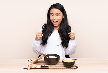 Teenager Asian girl eating asian food isolated on beige background celebrating a victory in winner position