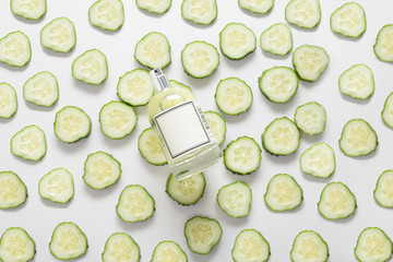The bottle is on cucumber circles, on a white background, top view, the cucumber is spread out all over the background. Concept of natural body oil, fresh perfumes, cosmetics, body care, fresh lotions