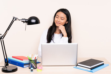 Student asian girl in a workplace with a laptop isolated on beige background looking to the side