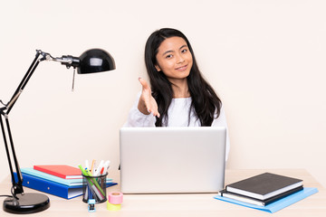 Student asian girl in a workplace with a laptop isolated on beige background shaking hands for closing a good deal