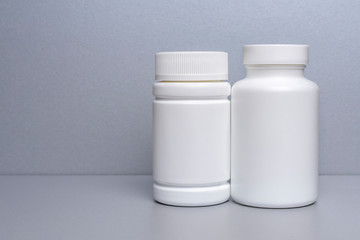 2 white jars for medicines and vitamins and dietary supplements without a name are on a gray shelf. copy space to the left. layout for a pharmacy, a store