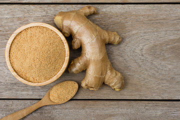 Fresh ginger powder in wooden bowl and spoon with ginger root isolated on wooden table background....