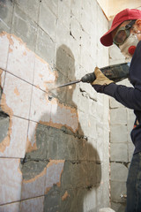 A working man with a hammer drill disassembles an old tile from a concrete wall.