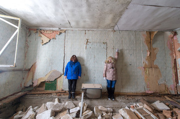 Nice young girl with her little sister in warm clothes stand against the wall in old room