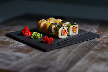 Sushi set on a square black plate of stone. Ginger and chopsticks are next to the set. Aged wood background