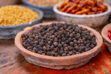 Indian spices collection, dried black peppercorns  and another spices in clay bowls