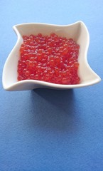 Red caviar of salmon fish in a white plate on a blue background.