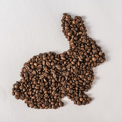Creative flat lay composition with easter bunny shape made of coffee roasted beans.Pastel colors and soft shadows. Realistic aesthetic look. Contemporary style.