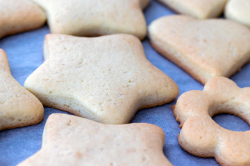 Baked shortbread cookies in the form of stars, hearts and flowers on a baking sheet with parchment paper just taken out of the oven. Tea snack for breakfast. Selective focus. Closeup view