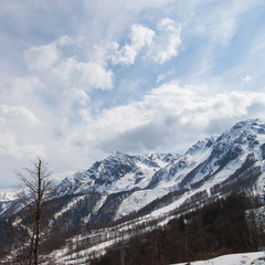 Peaks of snow-capped mountains against the blue sky with clouds