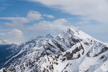 Peaks of snow-capped mountains against the blue sky with clouds