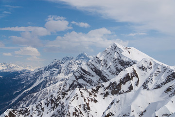 Peaks of snow-capped mountains against the blue sky with clouds