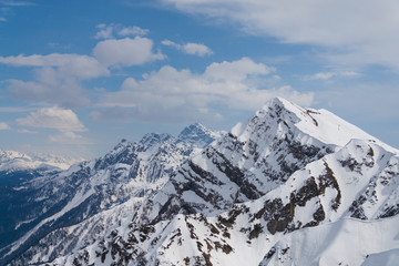 Peaks of snow-capped mountains against the blue sky with clouds