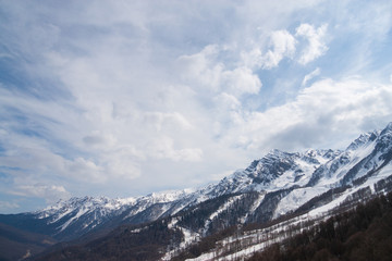 Peaks of snow-capped mountains against the blue sky with clouds