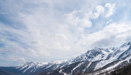 Peaks of snow-capped mountains against the blue sky with clouds