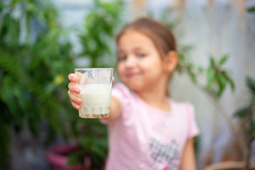 The girl holds forward a glass of kefir. Focus on the glass.